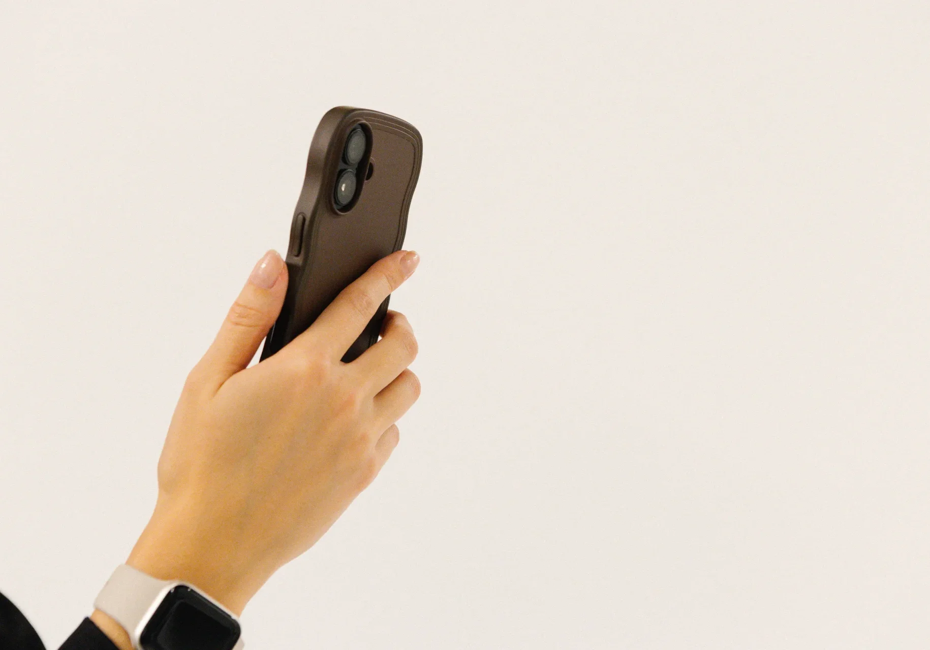 En person håller i en smartphone med mörkt fodral och har en smartklocka på handleden mot en vit bakgrund.